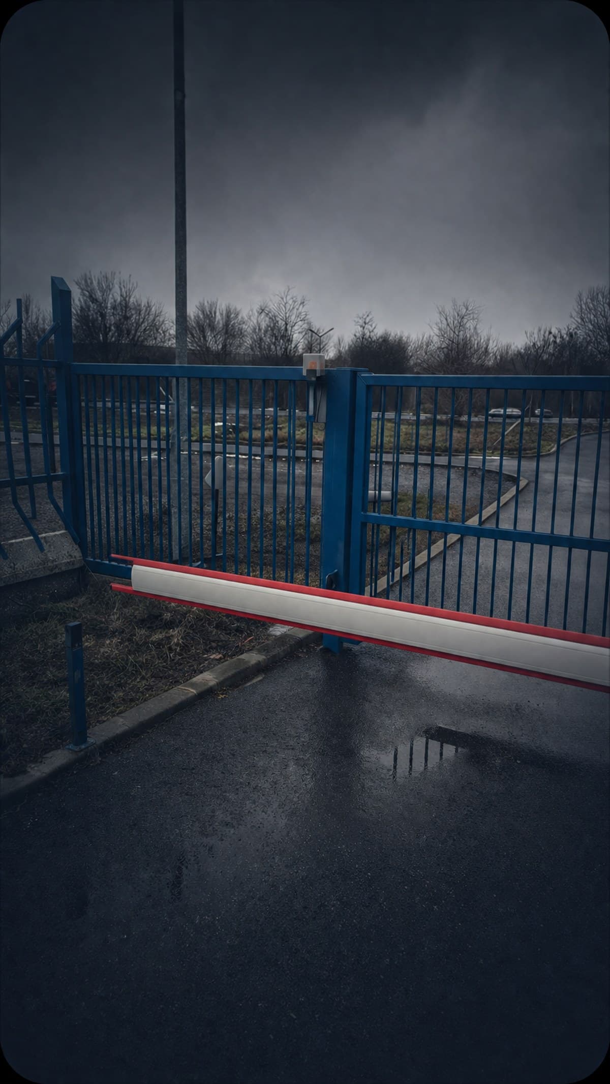 Barieră auto și poartă albastră de acces la intrarea într-o incintă, pe timp umed