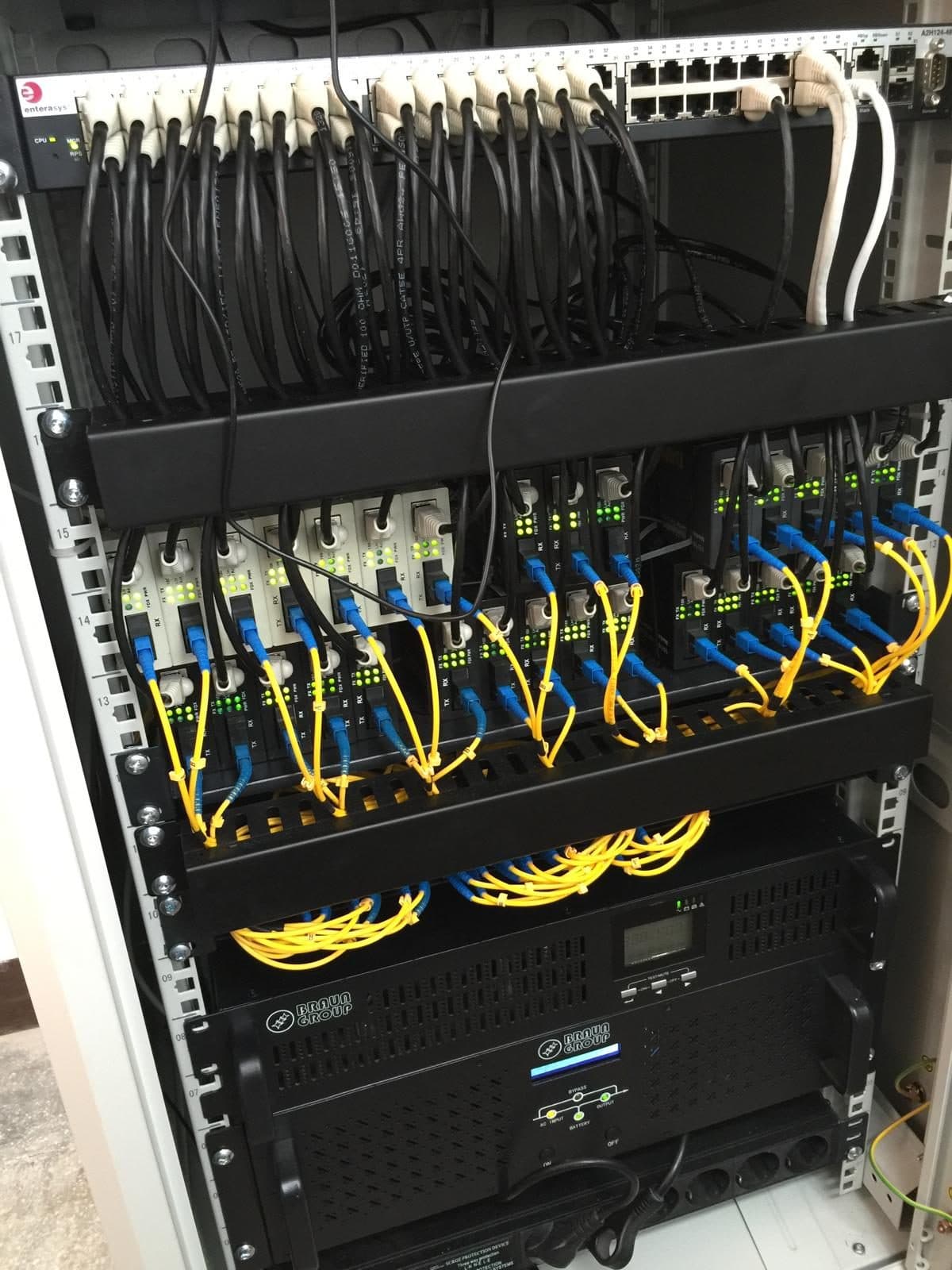 Rack de rețea cu patch panel-uri și cabluri organizate, într-o cameră de echipamente